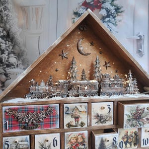 May include: A wooden advent calendar house featuring a top display with a train, pine trees, a moon, and stars. The lower section has numbered drawers decorated with vintage-style illustrations of children, winter scenes, and plaid patterns with floral accents.