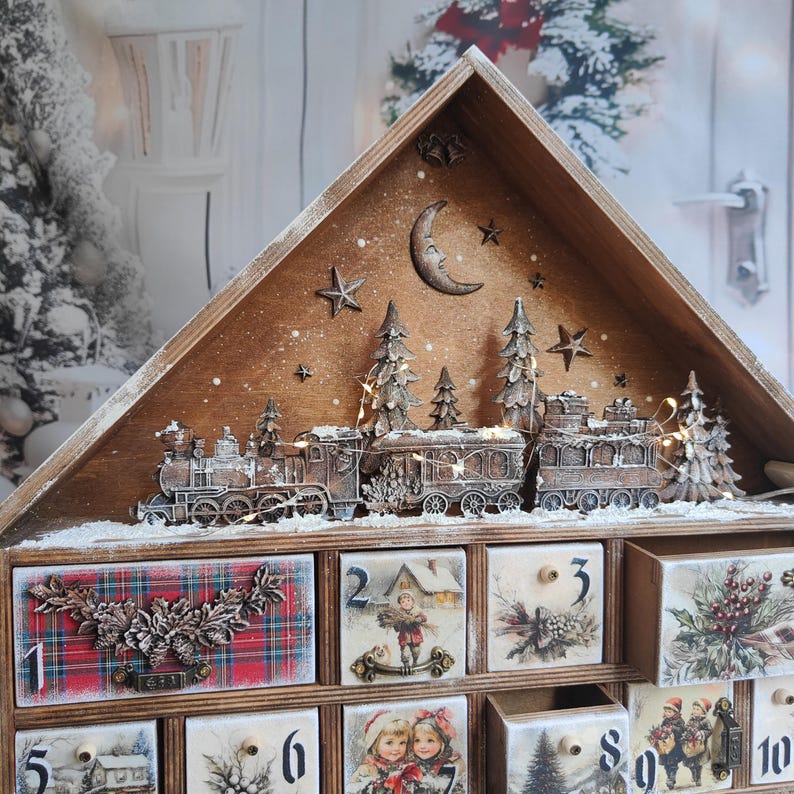 May include: A wooden advent calendar house featuring a top display with a train, pine trees, a moon, and stars. The lower section has numbered drawers decorated with vintage-style illustrations of children, winter scenes, and plaid patterns with floral accents.