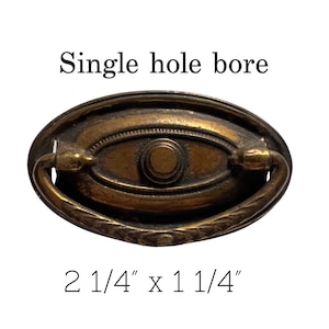 May include: A brass cabinet pull with a single hole bore. The pull is oval shaped with a decorative edge and a ring handle. The pull measures 2 1/4 inches by 1 1/4 inches.