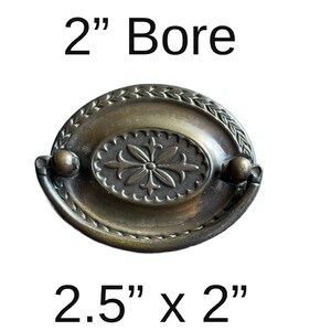 May include: A 2.5 inch by 2 inch oval brass cabinet pull with a decorative floral design. The pull has a 2 inch bore.