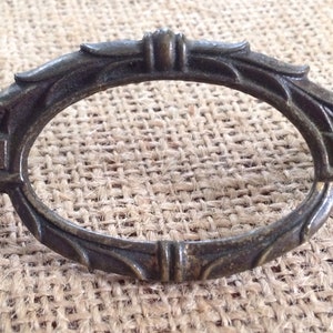 May include: An ornate oval-shaped metal pull with a decorative floral design. The pull is made of a dark metal with a slightly aged finish.
