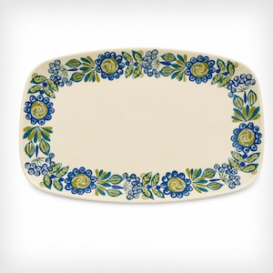 May include: A rectangular ceramic serving platter with rounded corners, featuring an off-white base color and a decorative border of blue and green floral patterns, including stylized flowers, leaves, and small berry clusters arranged in a repeating design.