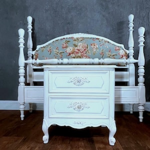 May include: White painted wooden nightstand with two drawers and ornate details. The nightstand has a scalloped base and sits on a wood floor.