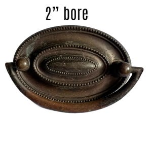 May include: A 2" bore antique brass cabinet pull with an oval design and a decorative beaded edge.
