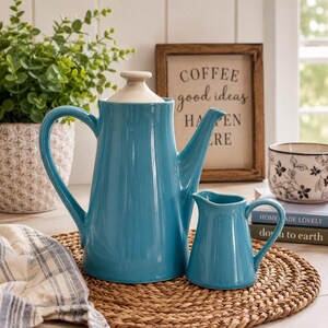 May include: A glossy turquoise ceramic coffee pot with a matching lid and a smaller turquoise ceramic creamer pitcher. Both pieces feature a smooth, solid-colored finish and curved handles, presented together as a coordinated set for serving.