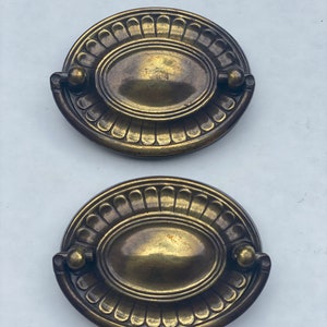 May include: Two antique brass oval cabinet pulls with a decorative, scalloped edge and a raised oval center.