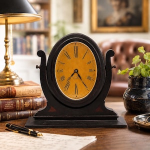 May include: An antique-style, oval-faced clock with a dark wooden frame. The clock face is a warm yellow with black Roman numerals. The clock has a decorative base and curved side supports. A classic desk clock.