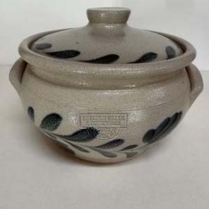 May include: A stoneware lidded pot with a light gray glaze and dark blue leaf designs. The pot has two handles and a lid with a knob. The text "Salmon Falls Stoneware 2002" is stamped on the front.
