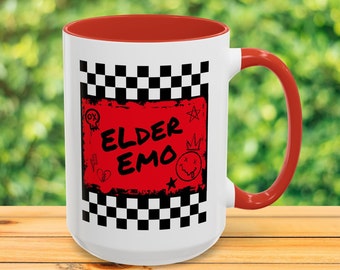 May include: White ceramic mug with a red interior and handle. The mug features a black and white checkered pattern with a red square in the center that says "Elder Emo" in black lettering. The red square is surrounded by black and white doodles.