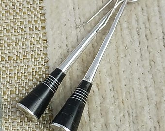 May include: A pair of silver-toned earrings with black, cone-shaped ends. The black ends have silver bands and a silver base. The earrings have a looped top and a long, thin, silver post.