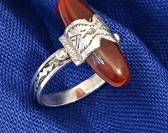 May include: A silver ring with a large, oval, reddish-brown stone. The ring features intricate silver detailing around the stone and on the band. The ring is set against a blue background.
