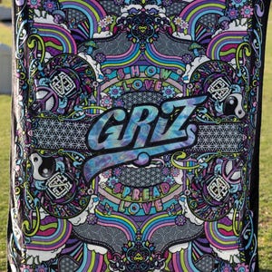 May include: A colorful blanket with a psychedelic design. The blanket features the word "GRiZ" in tie-dye lettering, surrounded by rainbows, flowers, and the phrases "SHOW LOVE" and "SPREAD LOVE". The border is black.