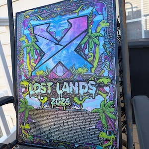 May include: A rectangular Lost Lands 2023 music festival poster featuring a large blue X logo, dinosaur illustrations, palm trees, and a detailed list of performing artists. The artwork uses a vibrant color palette of neon green, purple, and blue.