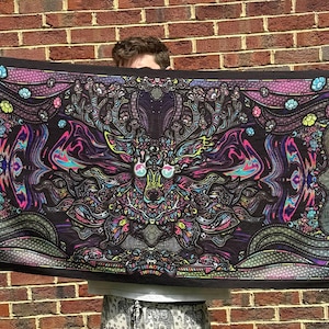 Puede incluir: Un tapiz negro con un diseño psicodélico que presenta un ciervo con ojos brillantes y patrones intrincados. El tapiz tiene la palabra "FOREST" escrita en ambos lados en una fuente colorida y estilizada.