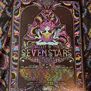 May include: A rectangular poster titled Valley of the Seven Stars featuring a central figure with multiple arms in a meditative pose. The artwork uses a vibrant color palette of pink, blue, and yellow against a black background with holographic details.