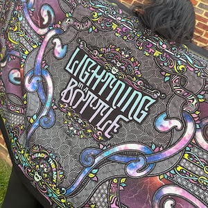 May include: A black textile with a colorful, psychedelic design. The text "LIGHTNING IN A BOTTLE" is prominently displayed in a stylized font. The design includes swirling patterns, vibrant colors, and the words "HEADY THREADS".