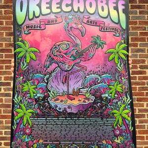 May include: A vibrant poster for the Okeechobee Music and Arts Festival. The design features a flamingo playing a guitar, set against a colorful backdrop with palm trees and waves. The poster includes the festival's name and dates.