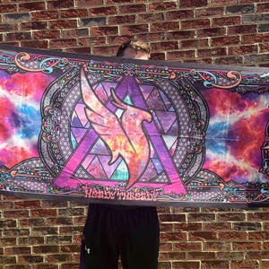 May include: A colorful tapestry with a vibrant design featuring a winged figure within a geometric shape. The tapestry showcases a blend of pink, purple, blue, and orange hues, with decorative borders and the text "Heavy Threads".