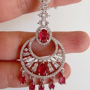 Może przedstawiać: Srebrny i czerwony kolczyk wiszący z dużym czerwonym kamieniem i mniejszymi czerwonymi kamieniami zwisającymi z dołu.