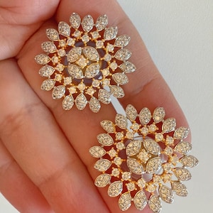 Könnte beinhalten: Ein Paar goldene Ohrringe mit einem runden Design, das mit einer Ansammlung kleiner, klarer Steine besetzt ist. Die Steine sind in einem zarten, floralen Muster angeordnet.