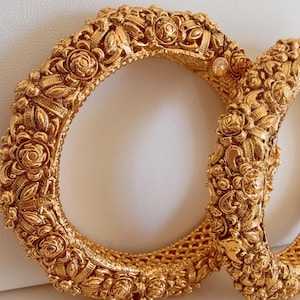 May include: Two gold-tone bangles with intricate floral designs. The bangles are stacked on top of each other.