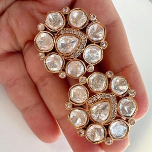 May include: A pair of gold earrings with a floral design. The earrings are made of gold and have a cluster of clear, faceted stones.