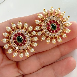 May include: A pair of gold earrings with a circular design featuring red, green, and white stones surrounded by white pearls.