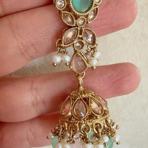 Pode incluir: Brincos dourados com uma pedra verde em forma de l&aacute;grima, p&eacute;rolas rosa e brancas e um pingente redondo dourado adornado com joias.