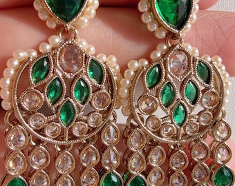 May include: Gold-toned chandelier earrings with emerald green and clear gemstones, accented with small pearls. The earrings feature a teardrop-shaped green stone at the top, with a series of dangling green and clear stones.