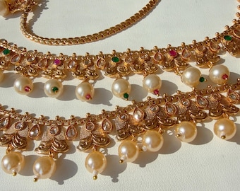 Pode incluir: Close-up de joias douradas com designs intrincados. As peças apresentam pérolas penduradas e pequenas pedras preciosas coloridas. As joias são provavelmente para uma ocasião especial, como um casamento ou um evento formal.