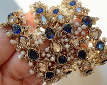 May include: Ornate gold bracelets featuring teardrop-shaped blue and clear gemstones, interspersed with small white pearls. The bracelets have a detailed design, with multiple gemstones and pearls.