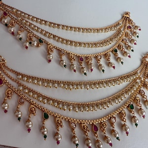 May include: A pair of gold-tone anklets with three strands of pearls and dangling charms. The charms feature green and pink gemstones.