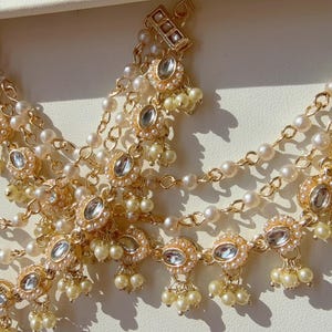 May include: Gold-toned headpiece with multiple strands of small pearls and decorative elements. The headpiece features clear, round gemstones and clusters of small, cream-colored pearls. The design is intricate and ornate, suitable for special occasions.
