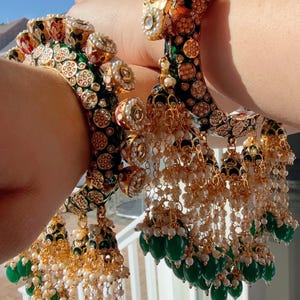 May include: Two ornate gold bangles with green and white enamel, pearl accents, and dangling green and white beads.