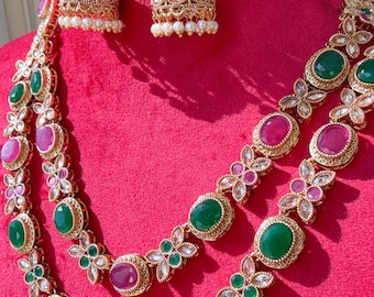May include: A gold-toned jewelry set featuring a necklace and earrings. The necklace has two strands with alternating green and pink oval gemstones, accented by floral designs. The earrings are bell-shaped with matching gemstones and pearl drops.
