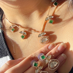 May include: A gold necklace and earrings set with a teardrop-shaped pendant and green stones. The pendant is surrounded by smaller diamonds.