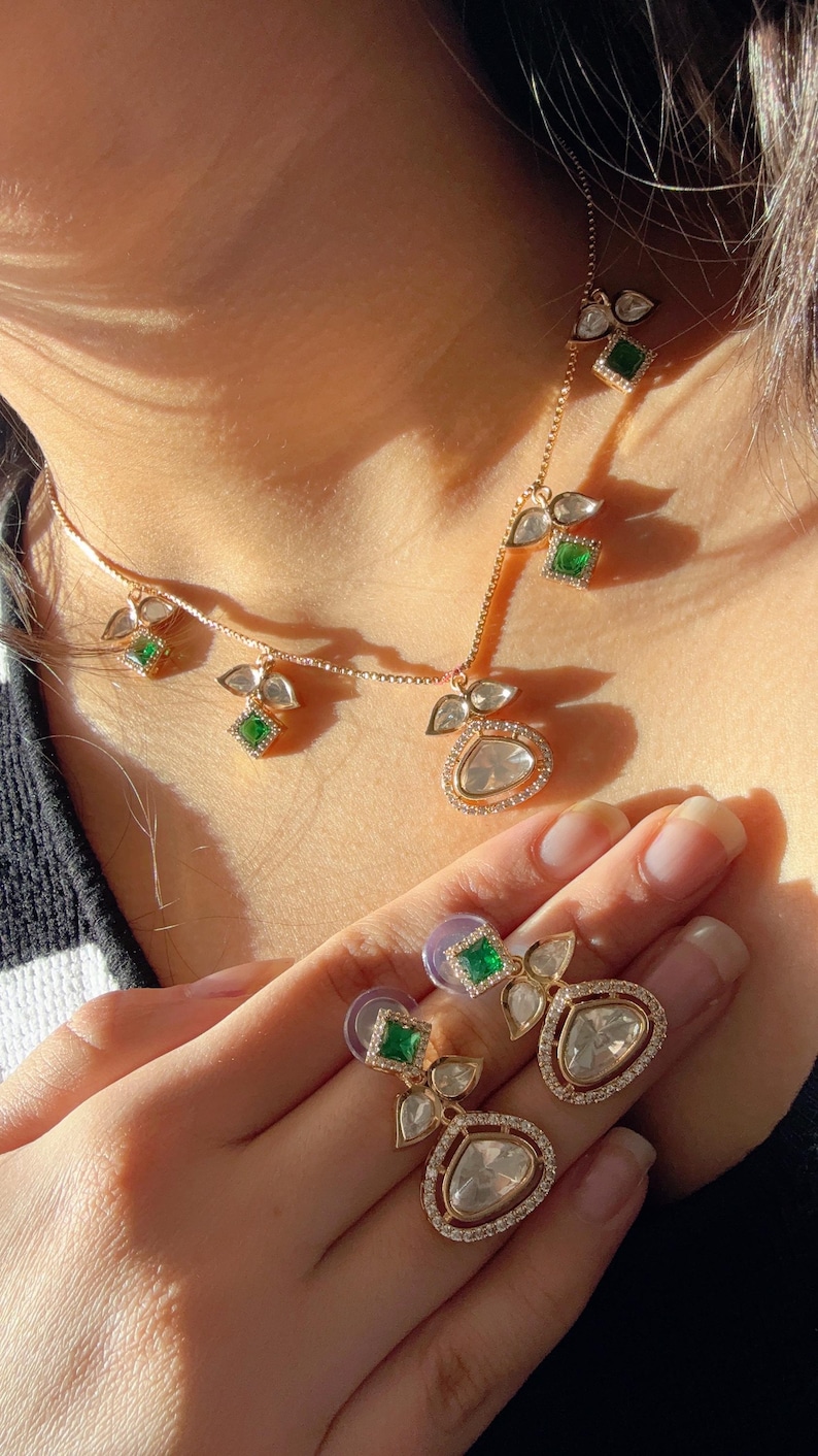 May include: A gold necklace and earrings set with a teardrop-shaped pendant and green stones. The pendant is surrounded by smaller diamonds.