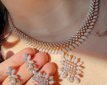 Peut inclure: Un ensemble de collier et boucles d'oreilles en or avec un motif floral. Le collier est composé de petits diamants scintillants et les boucles d'oreilles sont une paire assortie de clous en forme de fleur.
