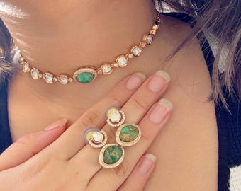 May include: A gold choker necklace with a green gemstone and clear stones. Matching earrings with green gemstones and clear stones.