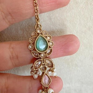 Pode incluir: Corrente de ouro com uma pedra verde em forma de l&aacute;grima cercada por strass transparentes, uma pedra rosa e p&eacute;rolas brancas.