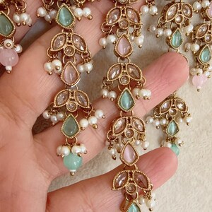 Pode incluir: Um colar de ouro com uma corrente delicada e v&aacute;rios pingentes. Os pingentes s&atilde;o adornados com pedras transparentes e de cor rosa e verde pastel. O colar &eacute; acentuado com pequenas p&eacute;rolas brancas.