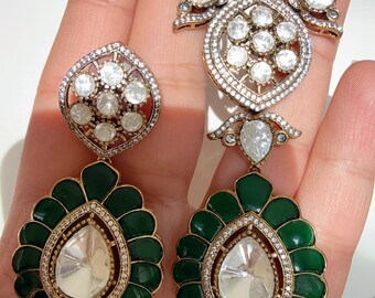 May include: A silver necklace and earrings set with a green enamel design. The necklace features a large pendant with a floral design and clear stones. The earrings are drop earrings with a similar floral design and clear stones.