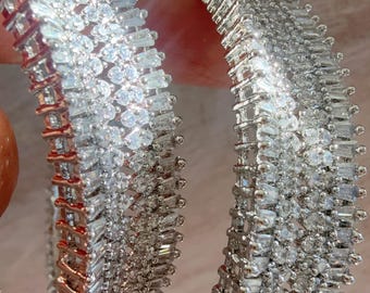May include: Two circular bangles featuring a dense arrangement of clear, baguette-cut and round-cut stones set in a metallic frame. The inner edge of one bangle displays a rose gold tone, while the outer surfaces are covered in reflective, sparkling stones.