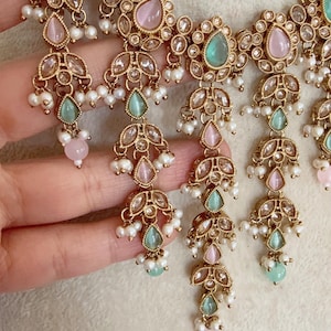 Pode incluir: Um colar de ouro com pedras rosa e verdes e detalhes de p&eacute;rolas. O colar tem um design em camadas com v&aacute;rias fileiras de p&eacute;rolas e pedras.