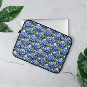May include: A laptop sleeve with a floral pattern featuring blue hydrangeas on a white background. The sleeve is black and has a zipper closure.