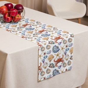May include: A white table runner with a repeating pattern of seashells, starfish, and crabs. The pattern is in shades of blue, brown, and red.