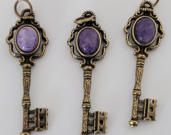 May include: Three antique-style key charms with purple gemstone accents. Each key features intricate details and a decorative design.