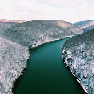 May include: Aerial view of a snow-covered forest with a winding river running through it. The river is a deep green color and the forest is covered in white snow.