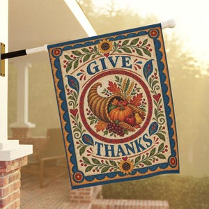 Puede incluir: Una bandera de jardín rectangular con un cuerno de la abundancia lleno de calabazas, maíz y uvas. El texto "GIVE THANKS" está impreso en azul. El diseño incluye girasoles, corazones rojos y follaje verde sobre un fondo crema con borde azul.