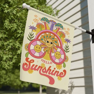 May include: A yellow and orange sun with a smiling face and sunglasses, surrounded by pink and white smiley faces and mushrooms. The text "Hello Sunshine" is written in a retro font.